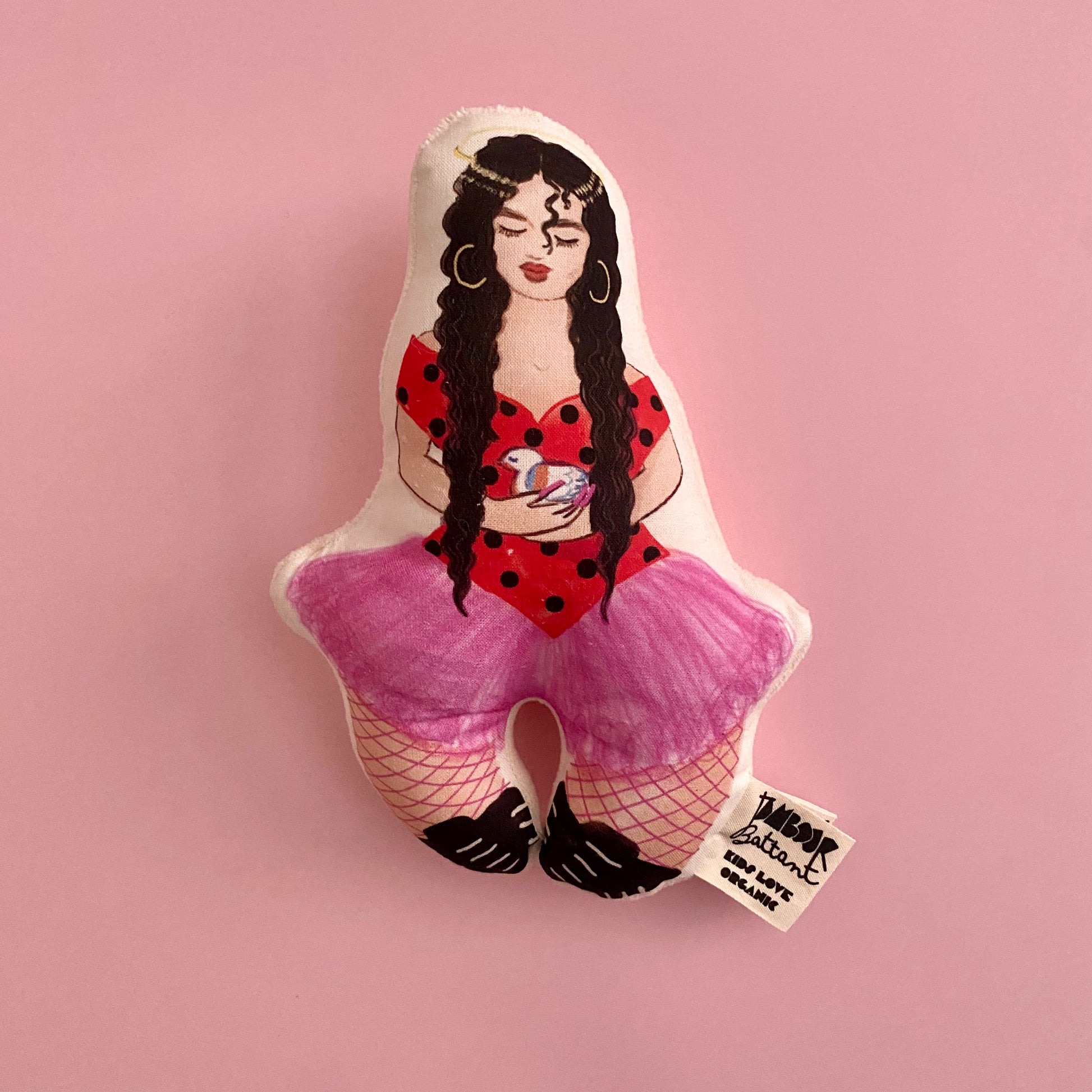 Poupée hochet, Rosalia dessiné à l'aquarelle. Le hochet est posé sur un fond rose uni.
