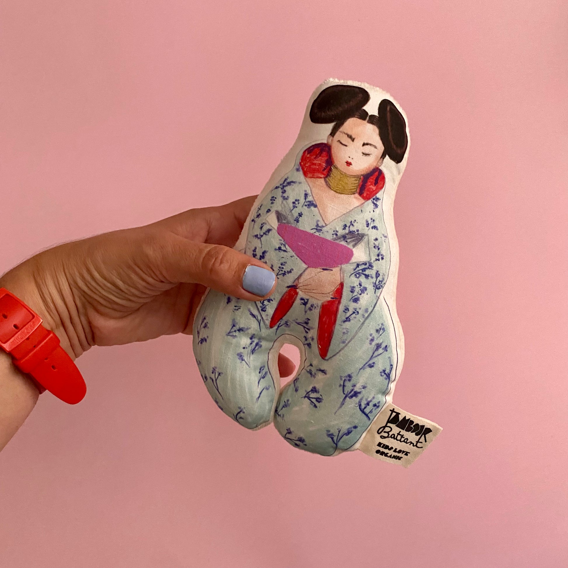 Poupee en tissu dans une main sur un fond rose