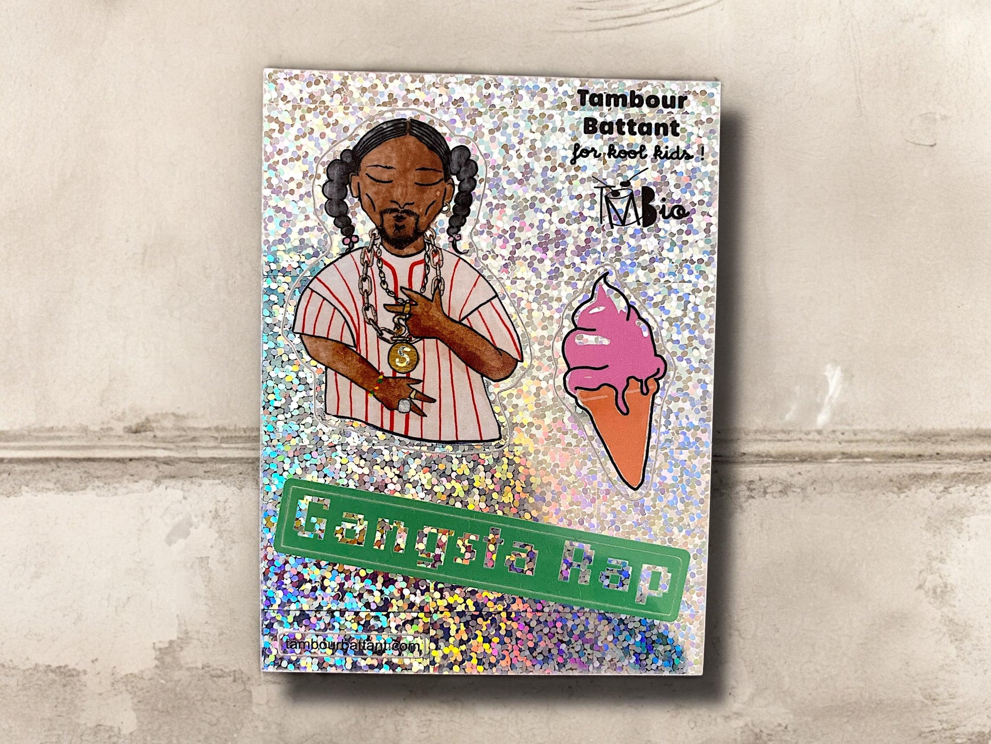 planche de papier holographique contenant 3 stickers : en haut à gauche, un dessin inspiré de snoop doggy dog, au milieu et à droite une glace à l’italienne rose, et en bas une bande verte avec le mot Gangsta rap en lettres pailletées.